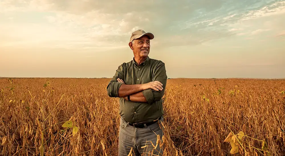 Farmer standing in a golden crop field, representing the agricultural producers served by American Drone Network
