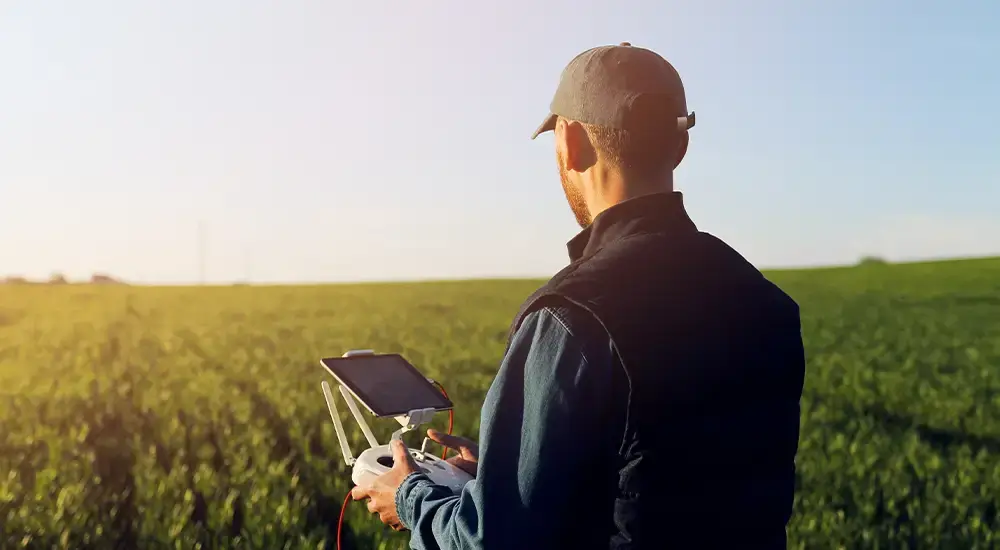 Agricultural drone pilot standing in a crop field operating a drone with a tablet controller