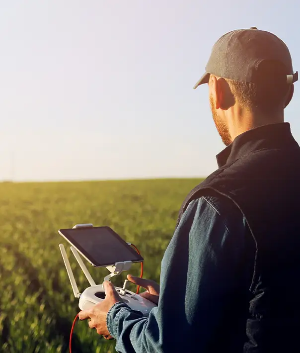 Agricultural drone pilot holding controller and tablet in a green crop field - join American Drone Network and find spraying jobs